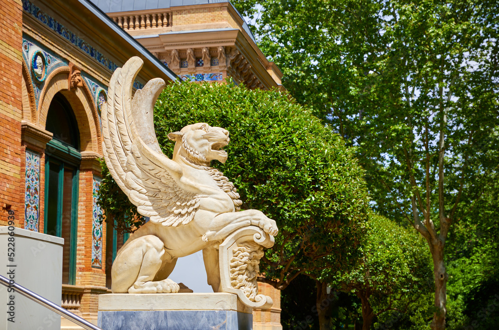 Madrid, Spain. Statue of Lion with wing by the entrance in Palacio de Velazquez Palace in Buen Retiro ParkParquepark(parque del Buen Retiro). Sunny summer day. Madrid, Spain. Statue of Lion with wing by the entrance in Palacio de Velazquez Palace in Buen Retiro ParkParquepark(parque del Buen Retiro). Sunny summer day.