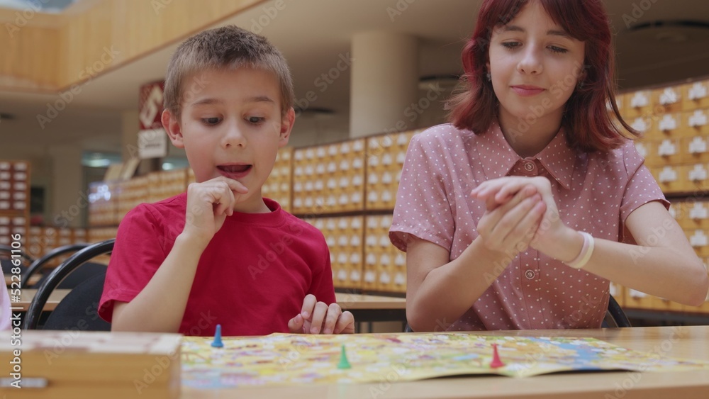 4K. Children play a board game in the library, sitting at the table. 4K. Children play a board game in the library, sitting at the table.