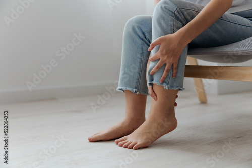 Closeup shot of pain leg calf suffering tanned beautiful young Asian woman touch ankle at home interior living room. Injuries Poor health Illness concept. Cool offer Banner