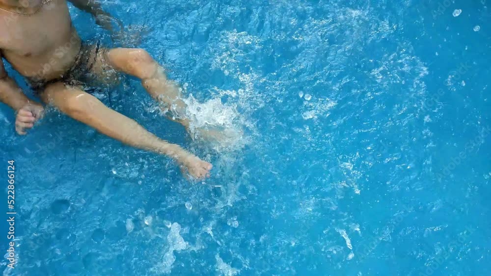 Boy splashing in water with his feet in the pool. Summer vacation concept. Water procedures in the summer in the pool. Boy splashing in water with his feet in the pool. Summer vacation concept. Water procedures in the summer in the pool.