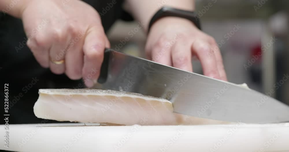 cutting cod cod fillet on a plastic board in professional restaurant kitchen. Close up arm with a knife 