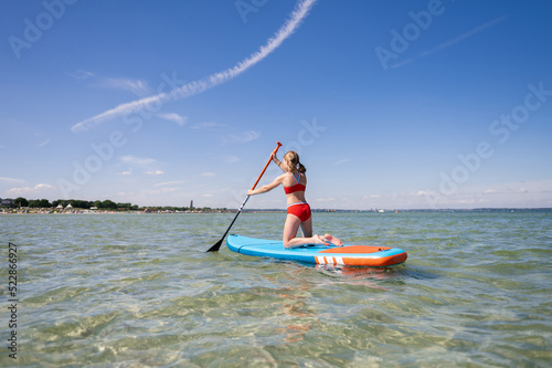 Beautiful child girl practice paddling on surfboard in sea at summer
