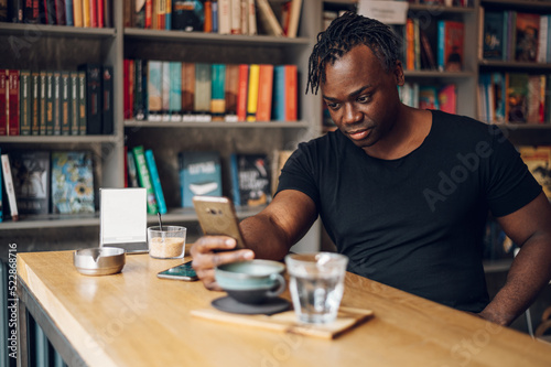 African american man using smartphone while drinking coffee in a cafe