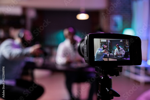 Content creator using camera to record podcast conversation, filming talking show discussion in studio. Social media vlogger chatting and broadcasting live, meeting with happy guest.