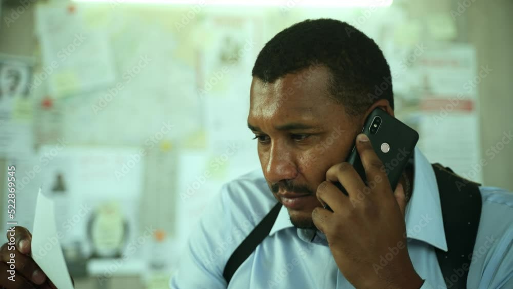 Close-up of concentrated male detective talking on phone while looking on investigation file. Serious african american fbi agent or policemen working on difficult case while sitting at the table. 4K 