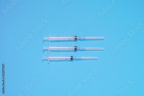 Three plastic disposable syringes lie on a blue background in the center of the composition  vaccination  preparation for injection  healthcare  immunization of the population