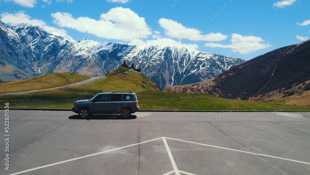 car on the parking near to Gergeti Trinity Church and great Caucasus mountains in the background, Kazbegi, Georgia. High quality photo