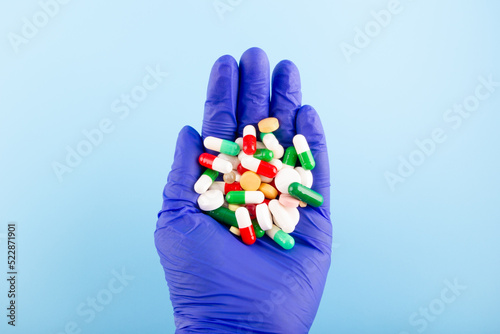 Hand in a blue medical glove with a handful of tablets and pills. Medicine concept.