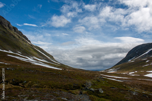 A hiking trail between Norwegian Nedalshytta and Swedish Sylarna mountain stations folowing a valley, early July, Jamtland, Sweden photo