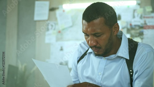Close-up of concentrated male detective reading investigation files at police department. Serious african american fbi agent or policemen working on difficult case while sitting at the table. 4K 