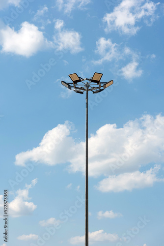 Tall metal lamppost with lamps in a circle against a blue cloudy sky - street lighting, LED lamps, energy saving