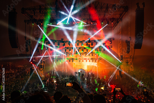 Horizontal Photo of the play of lights combined with fireworks while spectators record and photograph with their cellphone, picture of light show and pyrotechnics in a packed auditorium at night.