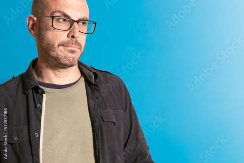 man with glasses, looking sideways, angry, worried, indignant. with a shirt. on blue background. copyspace.,