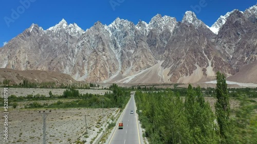 Cinematic drone shot of Passu Cones in Hunza Pakistan, moving towards the Tupopdan Peak with a Tuk Tuk driving on Karakoram Highway, wide aerial shot photo