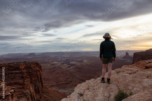 Adventurous Woman Hiking at a Desert Canyon with Red Rock Mountains. Cloudy Sunset Sky. Canyonlands National Park. Utah, United States. Adventure Travel © edb3_16