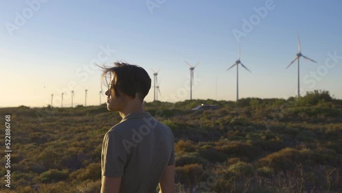 Young man watching wind turbines.
Man wearing glasses watching wind power plant at sunset.
