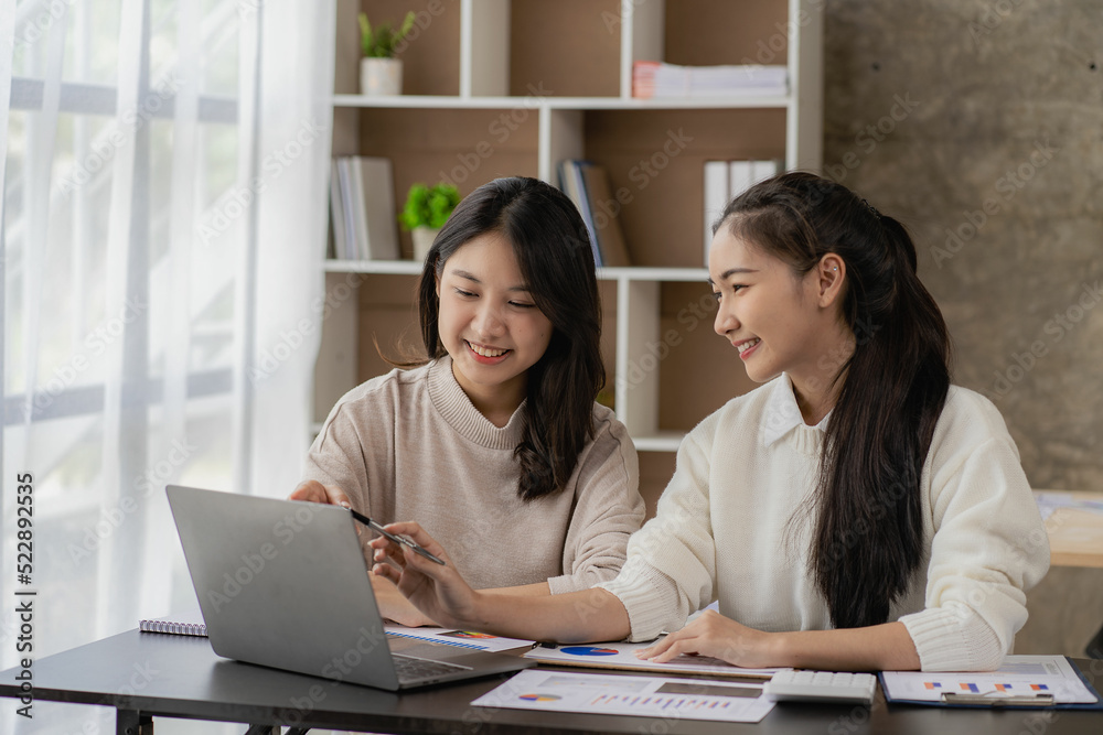 Two young Asian female accountants discuss working on investment projects and planning strategies using laptop computers in their office. Two young Asian female accountants discuss working on investment projects and planning strategies using laptop computers in their office.