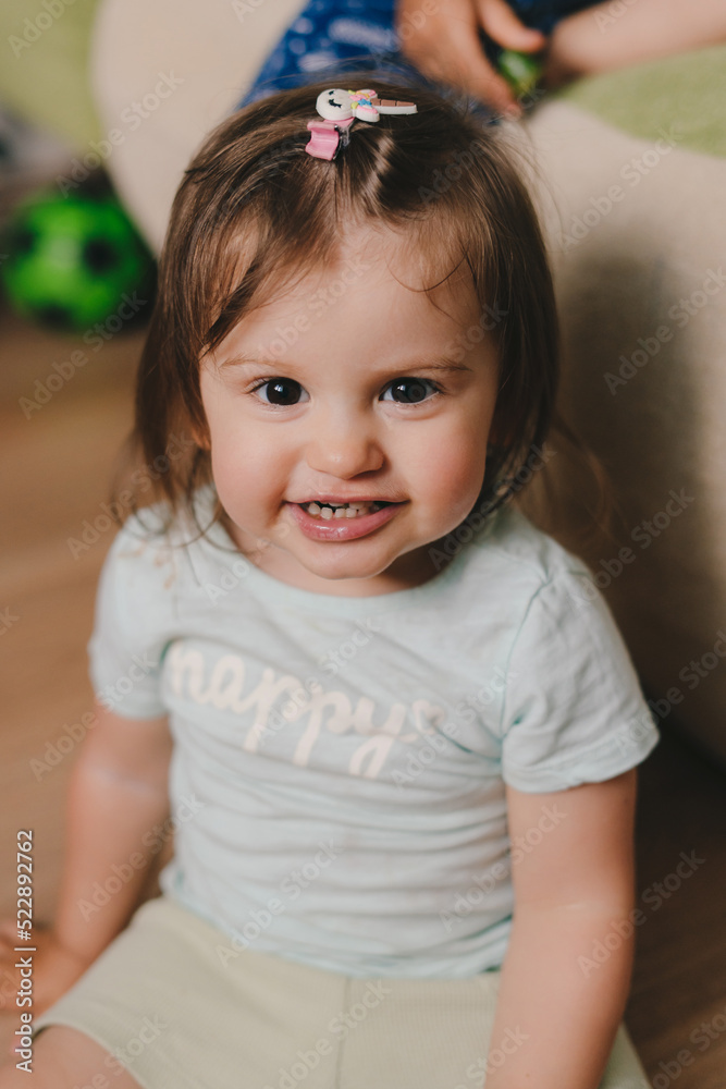 Smiling baby girl playing sitting on the floor and looking at camera. Happy family, childhood. Newborn baby care concept. Smiling happy child. Smiling girl. Smiling baby girl playing sitting on the floor and looking at camera. Happy family, childhood. Newborn baby care concept. Smiling happy child. Smiling girl.