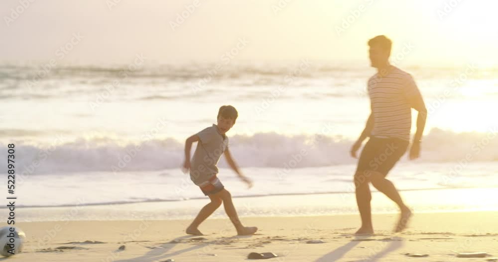 Active father and son playing soccer at the beach at sunset, having fun while keeping fit and bonding. Parent being playful with his child, enjoying a sporty game while spending free time together