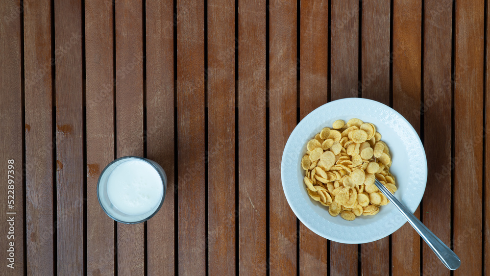 A plate of corn flakes on the right and a glass of milk on the left background A plate of corn flakes on the right and a glass of milk on the left background