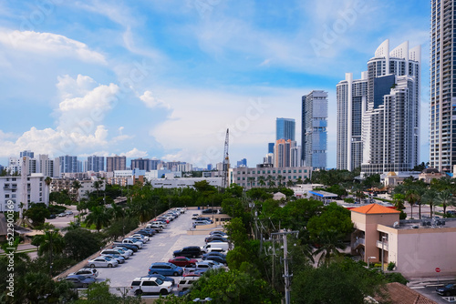 Panoramic aerial downtown city view with skyscrapers skyline, building roofs, trees and parking lot with cars top view against bright blue sky with clouds in summer day urban background photo.