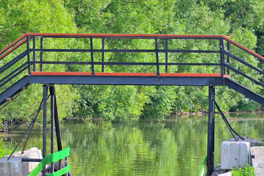 Metal pedestrian bridge over the river on a summer day Metal pedestrian bridge over the river on a summer day