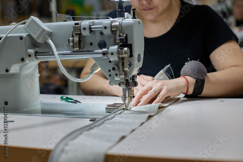 Seamstress or an employee of an Asian textile factory sewing on an industrial sewing machine. Close-up of the process of sewing fabric by a woman in production