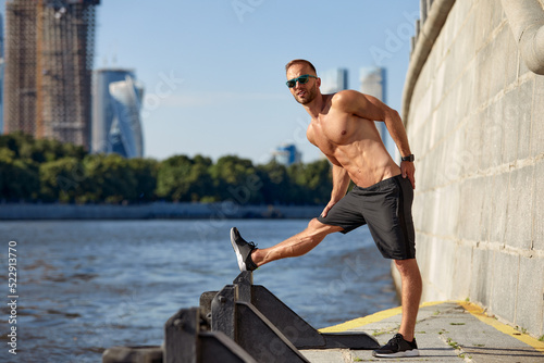 Athletic man running and doing functional workout outdoors - Sportive adult male with sportswear training in a city on the river bank © Georgii