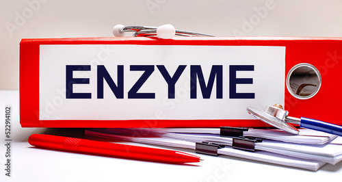 On the desktop is a stethoscope, documents, a pen, and a red file folder with the text ENZYME. Medical concept photo
