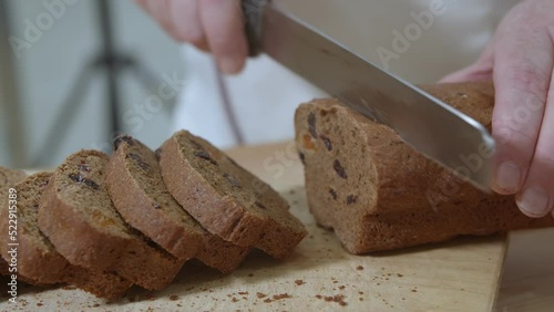 Baker is cutting baked Dutch bread with raisins and dried apricots with knife photo
