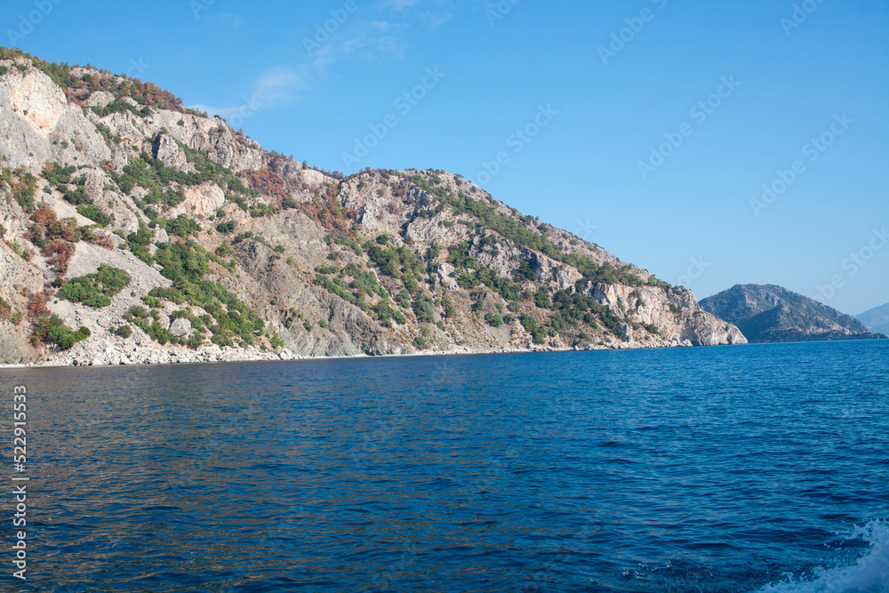 Mediterranean rocky shores with green trees and landscape. View from sea. Rock reflection in blue water sea.