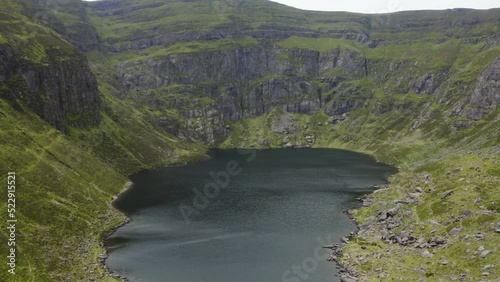 Coumshingaun Lough, Waterford, Ireland. Drone flies over the lake toward the cliffs. The lake is surrounded by mountains. Travel and hiking concept photo