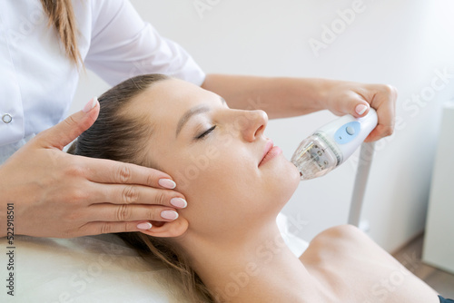 Handle radio frequency apparatus on chin woman's face during skin rejuvenation beauty lifting procedure. The beautician makes the hardware face of a woman of a cute woman. photo
