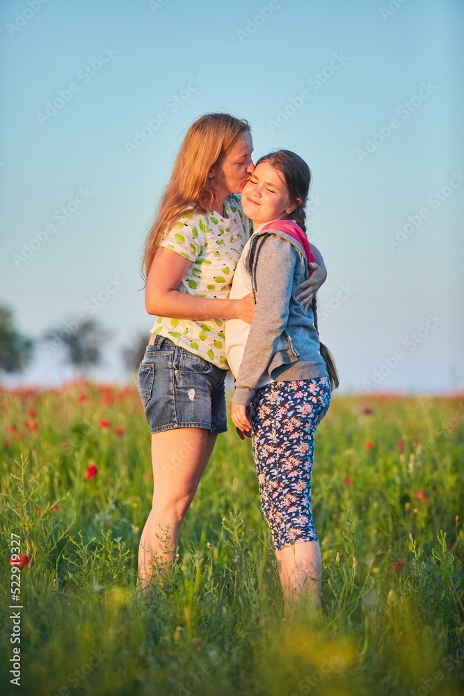 Mom and daughter are standing in a clearing with summer grasses at sunset. Mother's Day. Mom and daughter are standing in a clearing with summer grasses at sunset. Mother's Day.