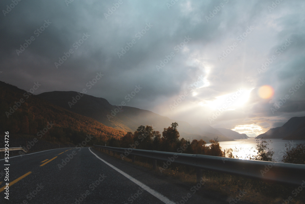 Rays of the setting sun illuminate the road. Spectacular sunset seen from a car window. Travel to Norway. Calm, inspiration and adventure.