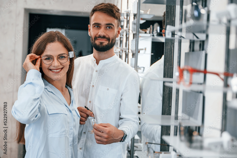 Standing and smiling. Man and woman in the glasses store. Helping to choose product Standing and smiling. Man and woman in the glasses store. Helping to choose product