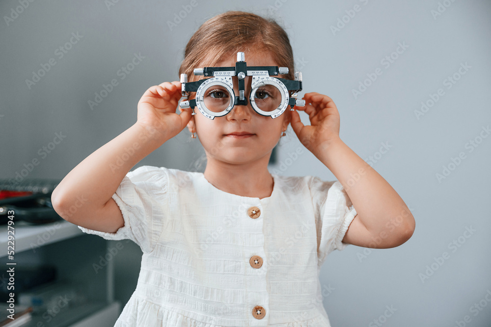 Looking forward with special device on the eyes. Little girl checking her vision by using special optometrist device Looking forward with special device on the eyes. Little girl checking her vision by using special optometrist device
