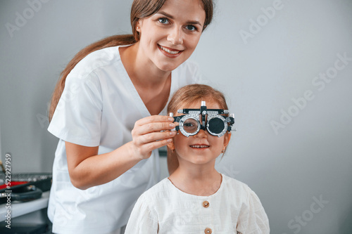 Looking forward, correcting eye sight by device. Little girl have their vision checking in the clinic by help of the female doctor
