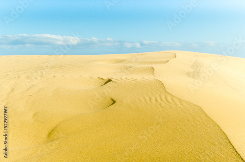 Sand dunes in a desert with blue sky and clouds in the background