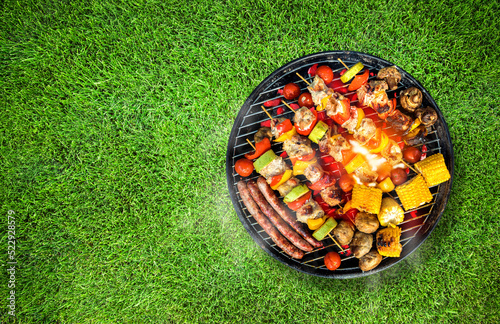 Top view of bbq grill, grilled meat, vegetables, mushrooms with flames and smoke. Placed on green grass lawn. Grilled food, copy space.