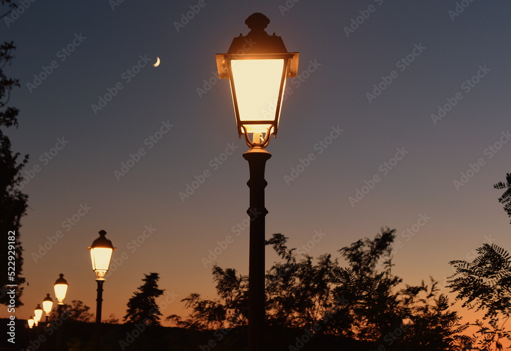 Reihe mit schmiedeeisernen Laternen vor Abendhimmel mit Mond