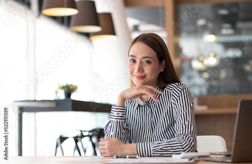 Charming Asian woman working at the office using a laptop Looking at the camera. © wichayada