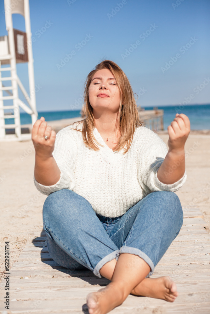 Plus size woman dressed jeans and white sweater walking in the city beach with sand against the sea