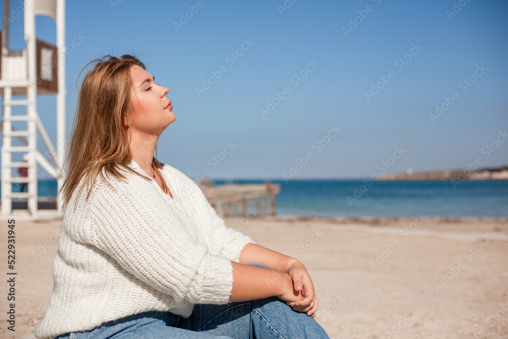 Plus size woman dressed jeans and white sweater walking in the city beach with sand against the sea