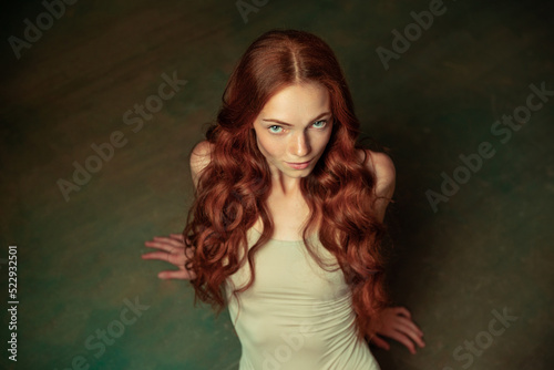 Fotografie Adorable tender redhead girl with long curly hair isolated over dark green background