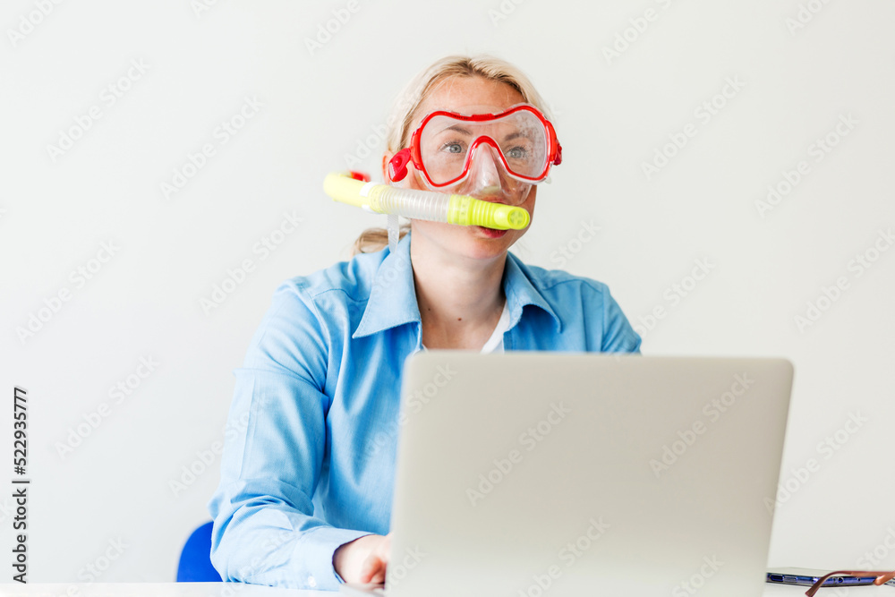 A blonde woman in a diving mask sits in the office, orders a tourist trip online, tickets for a plane, bus or train. Woman dreaming of sea at workplace A blonde woman in a diving mask sits in the office, orders a tourist trip online, tickets for a plane, bus or train. Woman dreaming of sea at workplace