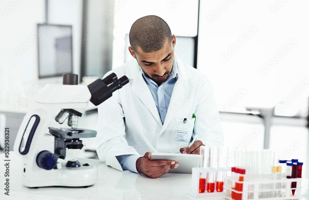 Scientist writing DNA results from microscope test on a tablet.Professional male doctor in a lab working with research tubes.Man in a modern laboratory doing medical science data analysis.
