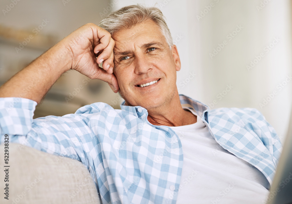 Handsome mature man relaxing on a sofa, casual, carefree and happy at home. Senior male enjoying the pleasure of retired life, satisfied and stressless. Older guy thinking, smiling and daydreaming
