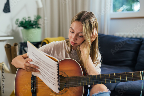 teenager reading songbook and playing acoustic guitar at home photo