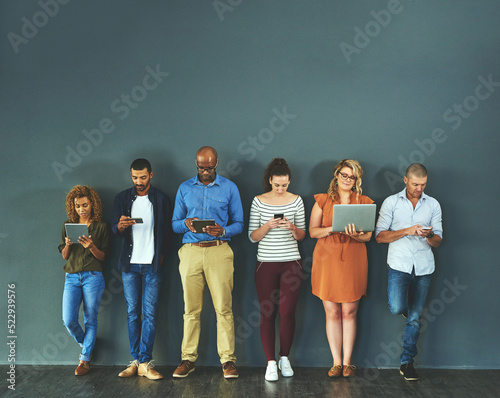 Diverse group of people browsing social media on a phone, tablet and laptop in studio on a grey background. Networking, surfing the internet and posting online with wireless technology and copyspace